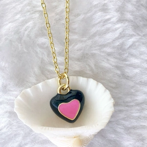 Detail of a gold necklace featuring a black and pink enamel heart pendant on white shells