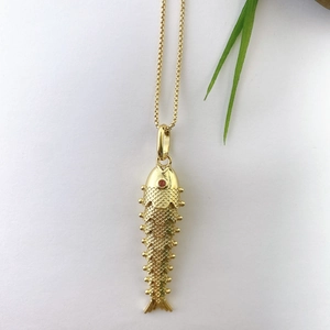 Detail of a gold-plated koi fish pendant with red gemstone eye and scales on white paper