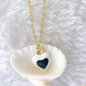 Detailed macro view of a gold-plated white and blue enamel heart pendant in a shell