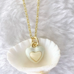 Macro shot of gold heart pendant with green enamel and white inlay on shell background