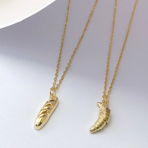Détail de colliers avec pendentifs croissant et baguette dorés en 3D sur chaînes fines