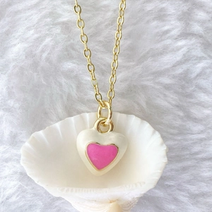 Detail of a 3D gold heart pendant with pink enamel inlay resting on a white shell