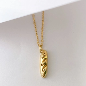 Gros plan d'un collier avec pendentif pain baguette doré en 3D et chaîne fine