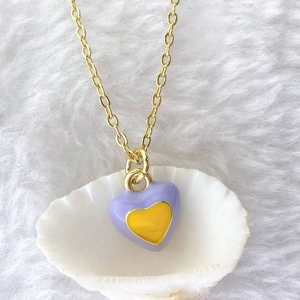 Detail of lavender heart pendant with yellow center in shell on white plush background