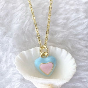 Detail of a gold heart pendant with blue and pink enamel finish inside a white shell