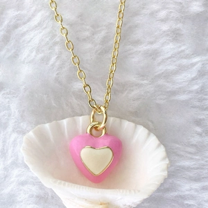 Close-up of pink and white enamel heart pendant on a gold chain inside a shell