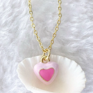 Detail shot of a pink enamel heart pendant on a gold chain inside a white seashell