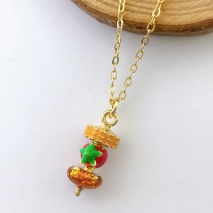 Detail of creative fruit charm necklace featuring apple and orange enamel pendants on gold chain