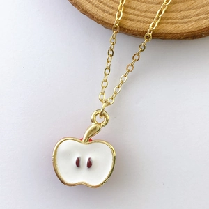 Close-up of apple pendant necklace with white enamel inlay and gold-plated metal detail