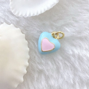 Macro detail of a light blue and pink enamel heart pendant with golden metal plating