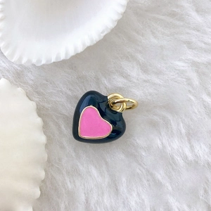 Detail of a black enamel heart pendant with pink center on soft white faux fur background