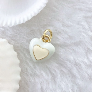 Detail of a white enamel heart pendant with gold plating on a soft plush background