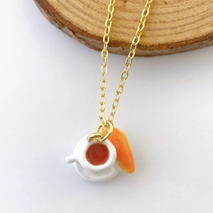 Macro detail of gold necklace with miniature coffee cup and croissant food pendants