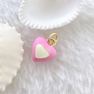 Detailed view of pink and white heart charm with gold ring on white plush surface