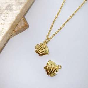 Macro detail of gold plated tropical fish charm pendants and necklace set on white stone