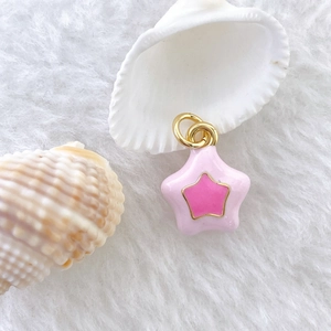 Close-up of pink enamel star pendant with gold-plated edges on a soft white faux fur background