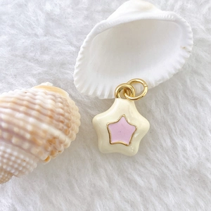 Macro view of cream enamel star pendant with gold ring on white plush texture