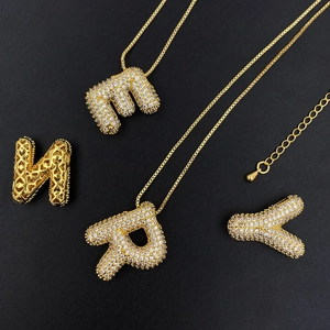 Close-up of golden bubble initial pendants with pavé zircon and heart cutout details