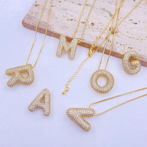 Golden bubble letter necklace with paved cubic zirconia on a minimalist stone background