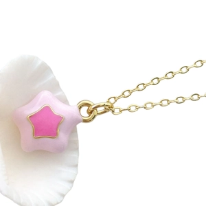 Pink enamel star pendant on gold chain necklace displayed elegantly on a white seashell