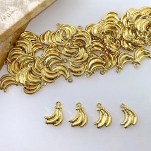 Macro detail of gold banana-shaped DIY jewelry charms on a white surface with travertine