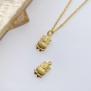 Macro detail of gold owl charm pendant with fine feather texture and cross chain link