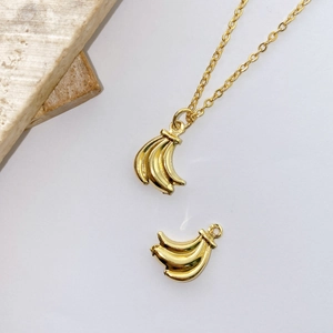 Detailed view of gold plated banana pendant set with thin chain on stone background