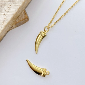 Macro detail of a polished gold-plated horn pendant necklace on white background