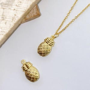 Detailed view of a gold-plated pineapple pendant with cross chain on a stone surface
