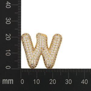 Detailed macro view showing a gold-plated letter W pendant with cubic zirconia next to a ruler