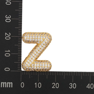 Macro shot of gold letter Z pendant with cubic zirconia next to a metric ruler