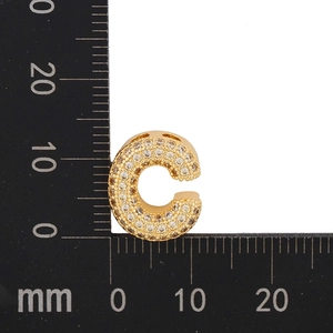 Macro shot of gold letter C pendant with pavé zircons next to a millimeter scale
