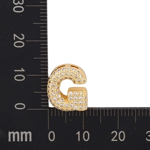 Macro view of gold-plated letter G pendant with cubic zirconia next to a metric scale