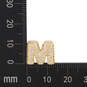 Macro shot of gold letter M pendant with paved zircons measured by a black ruler
