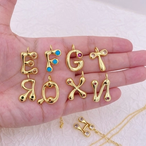 Detailed close-up of gold-plated alphabet pendants with colorful zircon stones on hand