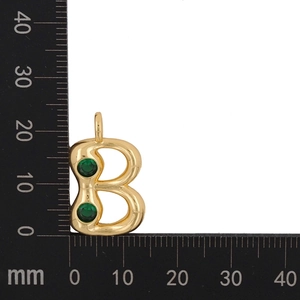 Detail shot of a gold-plated letter B pendant with green zircons on a metric ruler