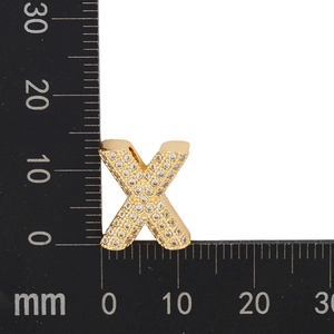 Macro shot of gold-plated letter X pendant with cubic zirconia and measurement ruler