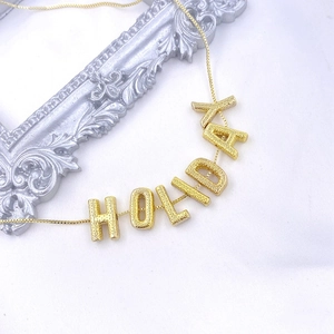 Detail of golden Holiday letter pendant with textured finish on white silk background