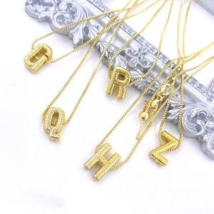 Macro detail of textured gold letter pendants with adjustable box chain necklaces