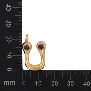 Macro shot of gold-plated U-shaped pendant with purple zircon stones on measuring scale