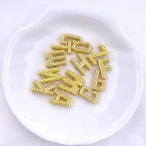 Macro shot of gold-plated alphabet charms with textured sandblast finish in a white dish
