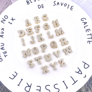Makroaufnahme von 26 Gold-Alphabet-Anhängern mit funkelndem Zirkonia auf weißem Teller