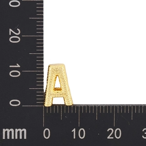 Macro shot of gold-plated letter A pendant with grainy texture measured on a metric ruler