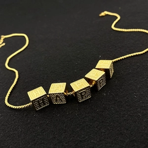Close-up of golden Happy cube letter pendant on a detailed twisted rope chain necklace