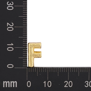 Detailed view of gold-plated letter F pendant with hammered texture next to a measuring tool