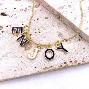 Détail d'un collier doré avec des pendentifs alphabet ENJOY en émail coloré