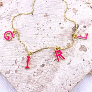 Détail d'un collier chaîne dorée avec charms lettres en émail rose épelant GIRL