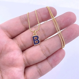 Détail d'un pendentif lettre B doré avec émail violet sur une chaîne délicate dorée