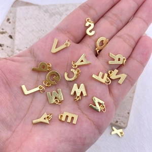 Détail de 26 pendentifs alphabet en émail coloré tenus en main pour bijoux DIY