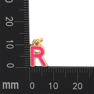 Gros plan du pendentif lettre R rose avec base dorée et règle de mesure de 12 mm